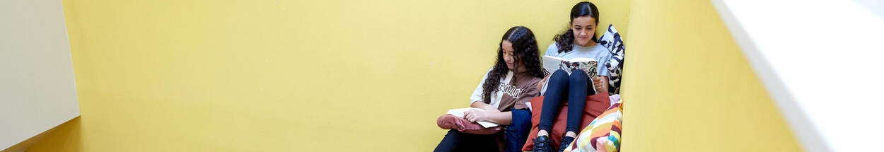 2 meiden uit groep 8 lezen op een speelse manier op een schooltrap