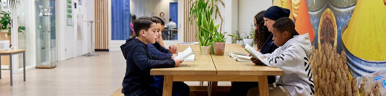 Basisschoolkinderen aan een lange tafel, samen aan het lezen