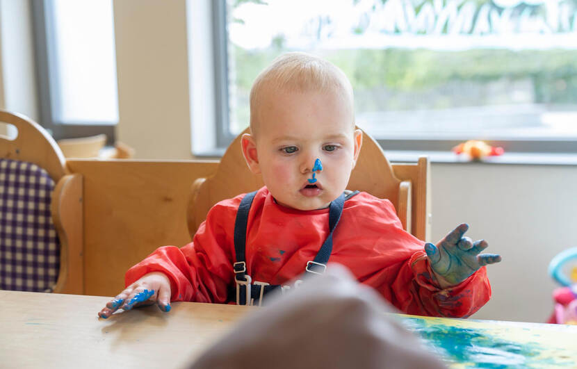 Kindje speelt met vingerverf en heeft blauwe verf op de handen en neusje