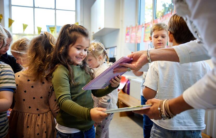 Meisje in de klas krijgt een boek aangereikt door de leraar